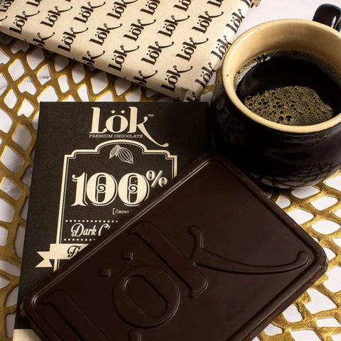 Dark chocolate bar with 'lok' branding next to a cup of coffee on a decorative surface.