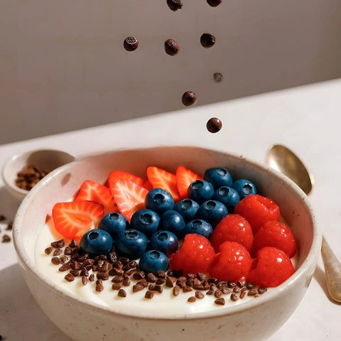 Yogurt bowl with strawberries, blueberries, and cherries being sprinkled with chocolate chips.
