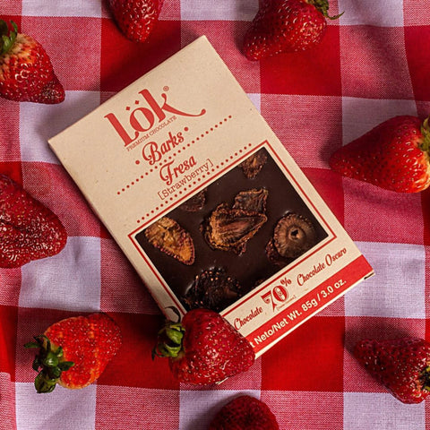 Box of Lök Strawberry Chocolate Barks on a red and white checkered tablecloth with strawberries around.