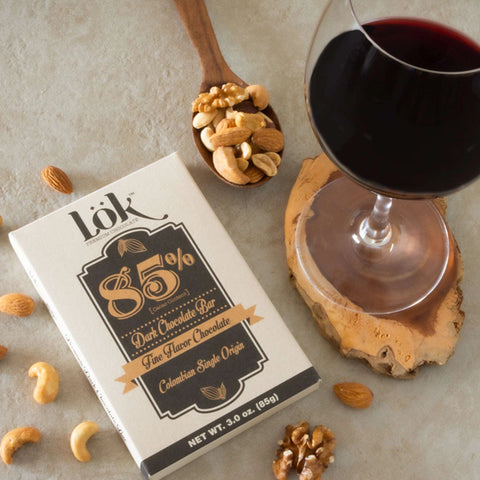 Lök 85% dark chocolate bar with a glass of red wine and nuts on a wooden coaster.